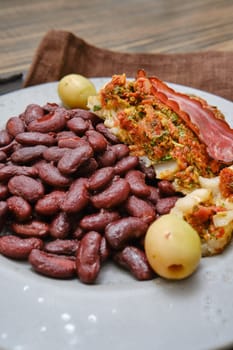 A plate features a hearty portion of red beans paired with stuffed meat that includes herbs, vegetables, and slices of cured meat. Green olives add a touch of acidity to the meal.