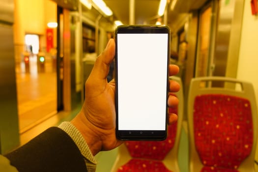 A person holds a blank smartphone while sitting in a subway car.