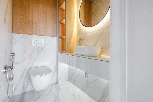 This contemporary bathroom showcases minimalistic design with marble walls and a circular mirror, emphasizing clean lines. A wall-mounted toilet and vessel sink add to the sophisticated aesthetic.