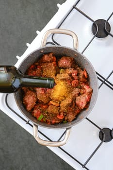 A pot filled with diced meat, chopped vegetables, and spices is being prepared on a sleek stovetop. Red wine is gently poured in to enhance flavours, creating a deliciously aromatic meal.
