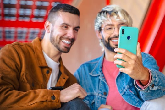 Two cheerful friends smile while taking a selfie with a smartphone. Bright colors and modern architecture create a vibrant urban vibe. Casual clothing and joyful expressions in daylight scene.