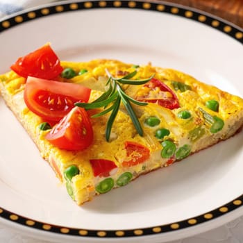 A slice of vegetable frittata featuring peas, red peppers, and herbs sits attractively on a decorative plate. Fresh tomato slices are garnished on top, adding color and flavor.