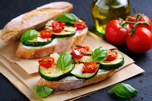 Delicious bruschetta features grilled zucchini and cherry tomatoes topped with fresh basil on crusty artisan bread. Placed on a rustic surface, olive oil and tomatoes add to the inviting atmosphere.