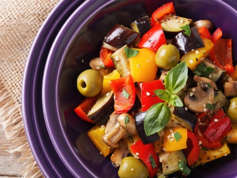A vibrant salad filled with diced bell peppers, eggplant, mushrooms, and olives is beautifully presented in a deep bowl. Fresh herbs garnish the dish, showcasing the abundant colors and fresh flavors.
