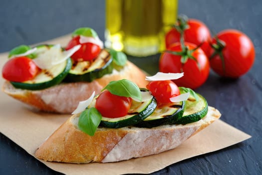Freshly made bruschetta features toasted bread topped with grilled zucchini, cherry tomatoes, and basil, all drizzled with olive oil. The cozy kitchen background adds warmth to the setting.