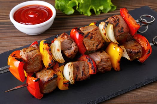 Grilled beef and colorful bell peppers skewered with onions create a vibrant dish. Served on a stylish slate platter, the meal is accompanied by a small bowl of dipping sauce, perfect for gatherings.