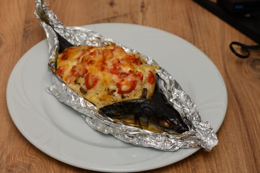 A beautifully prepared whole fish, wrapped in shiny foil, emerges from the oven, topped with a medley of tomatoes and melted cheese. This dish is perfect for a comforting dinner at home.