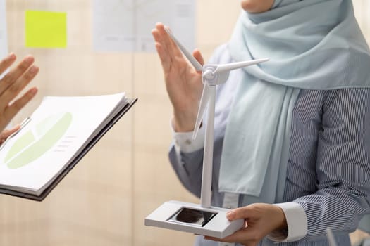 A woman explains the importance of wind energy using a model during a meeting, illustrating the impact of sustainable practices on business decisions.