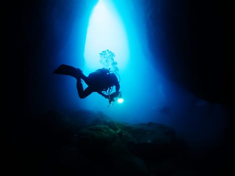 scuba diver diving inside a marine cave that illuminate with a flashlight, concept of active leisure lifestyle and underwater adventure, copyspace for text