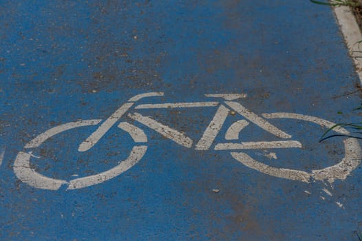 A fresh, white bicycle symbol stands out on a bright blue path, inviting cyclists to enjoy a journey through this urban environment. Sunlight bathes the area, enhancing the cheerful atmosphere.