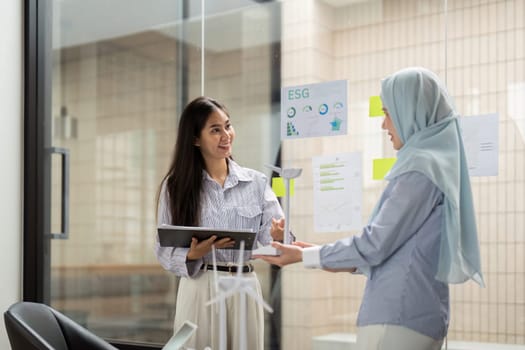 Two women communicate at their workplace about ESG strategies and sustainability measures, highlighting how renewable energy contributes to corporate responsibility and social impact.
