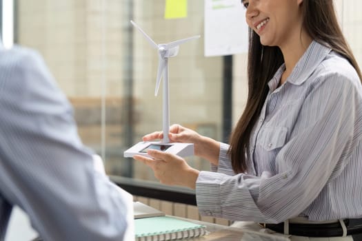 In a strategy meeting, a professional presents a wind turbine model while explaining the importance of sustainable energy solutions and ESG practices for future projects.