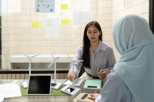 Two professionals engage in a productive meeting, focusing on ESG strategies and sustainable energy solutions. They analyze wind turbine models and discuss environmental initiatives.