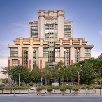 The majestic Ministry of Plantation Industries and Commodities stands tall in Putrajaya, Malaysia, surrounded by colorful flags and lush greenery, showcasing its impressive architecture at sunset.