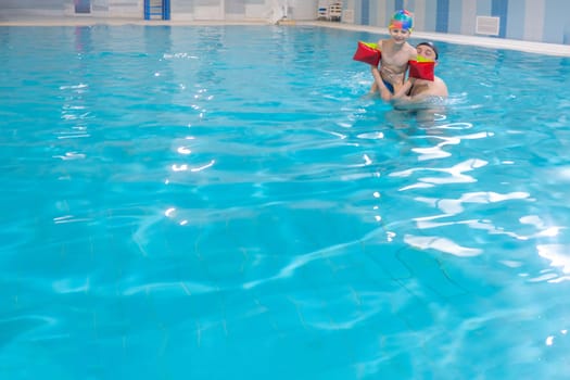 Happy middle-aged father swimming with cute adorable baby in swimming pool. Smiling dad and little child, boy having fun together. Active family spending leisure and time in spa hotel. Concept of kids sport, family summer vacation. Concept of healthy holiday and family activity