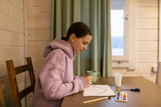 A young girl sits at a wooden table, focused on painting with watercolors inside a cozy cabin. Sunlight filters through the window, creating a peaceful ambiance.