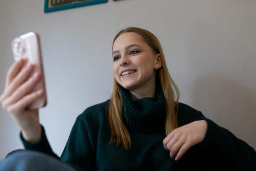 A girl with long hair sits comfortably at home, smiling as she interacts with friends on her smartphone, reflecting joy and connection during a casual moment.