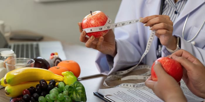 During a nutrition discussion, a medical professional measures apples to illustrate portion sizes while discussing healthy eating habits with a patient.