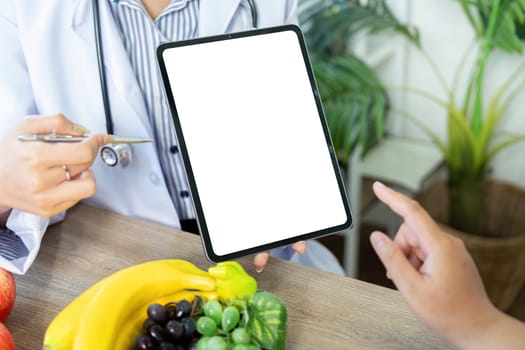 A nutritionist demonstrates meal planning on a tablet, visually engaging the patient to discuss healthy food choices alongside colorful fruits.
