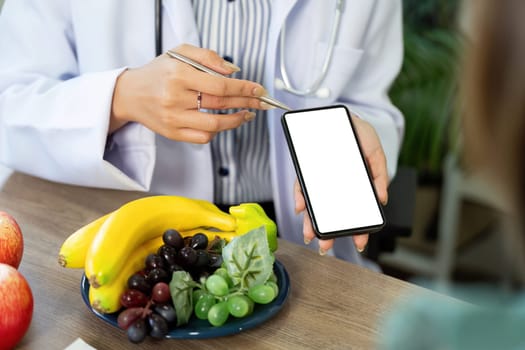 A doctor highlights dietary information on a smartphone while showcasing fresh bananas and grapes to guide a patient towards healthier eating.