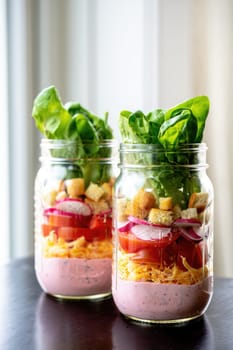 Colorful mason jars filled with layers of fresh salad ingredients, showcasing lettuce, tomatoes, croutons, and a creamy dressing. Perfect for a quick, healthy lunch or picnic idea.