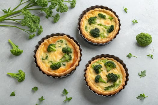Three freshly baked broccoli quiches sit in tart pans, garnished with green herbs. The light colored background enhances the appetizing look of the dish. Perfect for a savory snack or brunch.