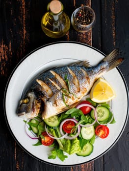 A beautifully plated whole grilled fish is accompanied by a vibrant salad of mixed greens, tomatoes, and cucumbers. Lemon wedges and herbs add a refreshing touch.