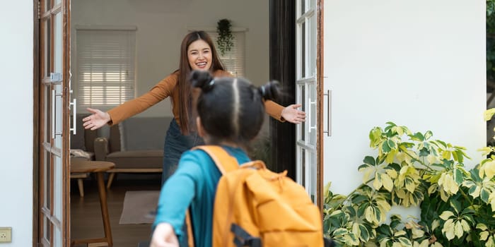 After a day at school, a girl joyfully rushes to her mother, who greets her with open arms. This moment captures the excitement and love shared between them.