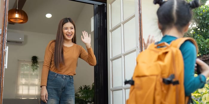 As the daughter heads off to school, her mother waves with a bright smile. The image symbolizes love, encouragement, and the start of an educational journey.