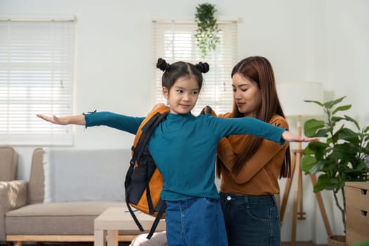 In a loving gesture, a mother helps her daughter put on her backpack, ensuring it's properly adjusted for a day full of learning and fun.