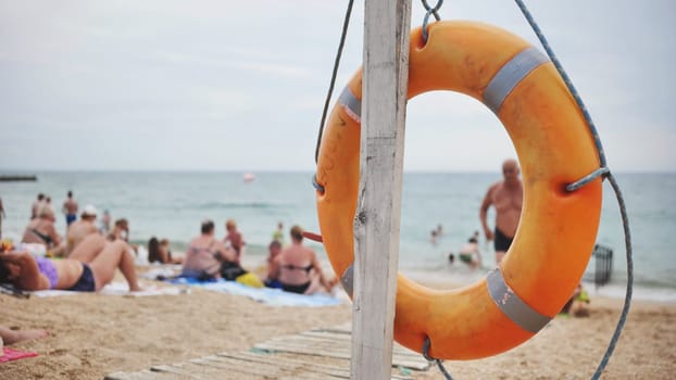 Bright orange lifebuoy on a sandy beach in crimea, black sea, with people relaxing and enjoying the sunny day by the water
