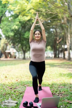 Engaging in yoga, a young woman focuses on her balance and inner peace amidst nature, embracing a routine that promotes wellness.