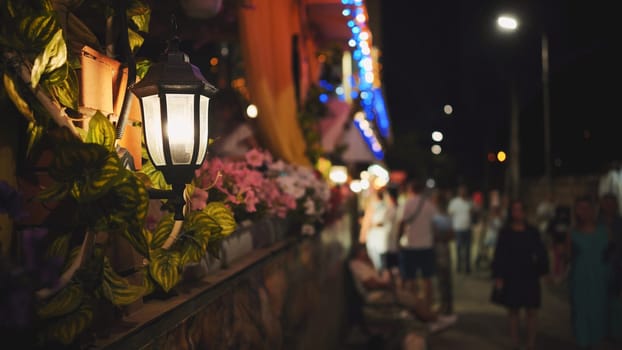Warm light from a street lamp illuminates a lively night scene in crimea, with blurred figures enjoying the black sea atmosphere