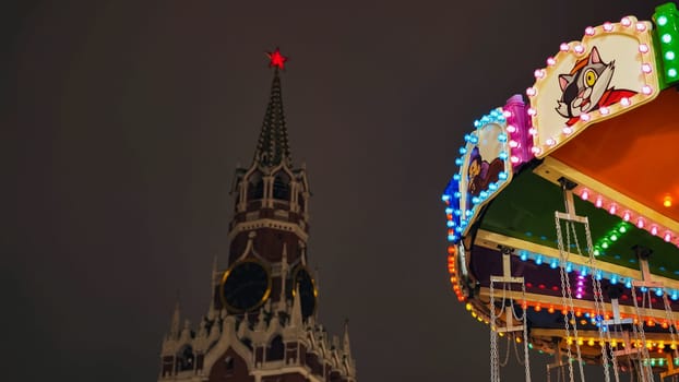Brightly lit carousel with Spasskaya Tower in the background during Moscow Christmas festival