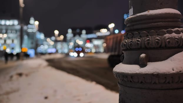 Snow covering ornate lamp post in Moscow at night with blurred background of buildings and traffic