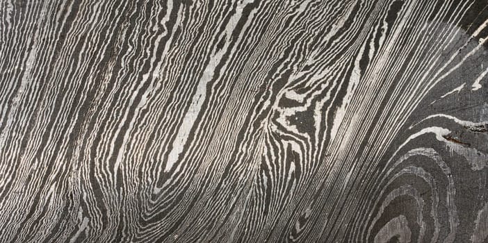 Detailed close up of damascus steel, showcasing its characteristic wavy and layered pattern of light and dark metal. Texture is intricate and unique