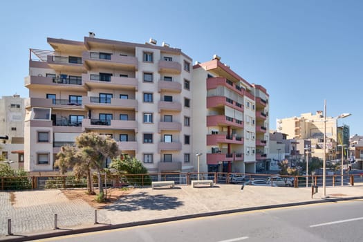 Crete.Greece - april 11, 2025: A sunny urban street in Crete featuring modern apartment buildings, balconies, and parked cars. The clean environment and contemporary architecture highlight everyday city life.