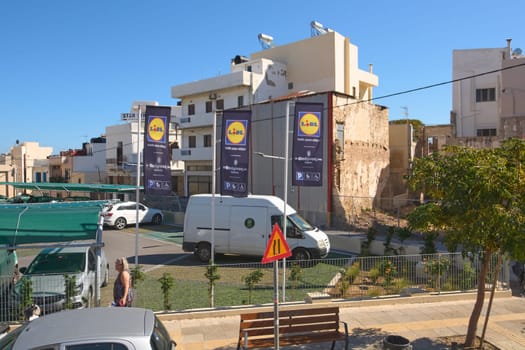 Crete.Greece - april 11, 2025: Exterior of a Lidl supermarket featuring prominent banners with Greek text. The parking area is busy with cars and pedestrians, reflecting a typical urban shopping experience.