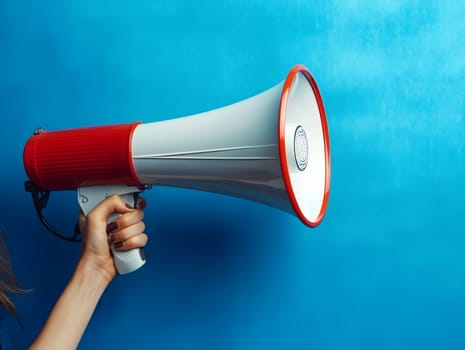 Close-up of a person’s hand gripping a classic red and white megaphone in front of a vibrant blue wall, symbolizing speech, protest, marketing, or announcement, bold visual composition, AI generated