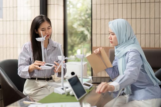 In a modern office, the two team members strategize on sustainable practices using visual aids, aiming to innovate solutions that promote environmental stewardship.
