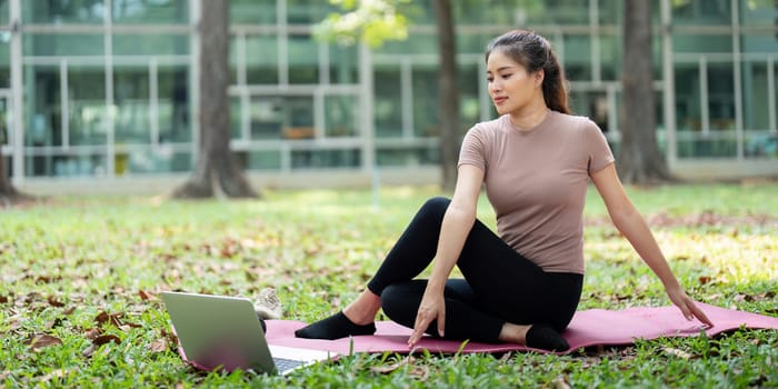 A focused woman attentively follows an online workout session on her laptop in an outdoor setting, embodying her commitment to a wellness routine.