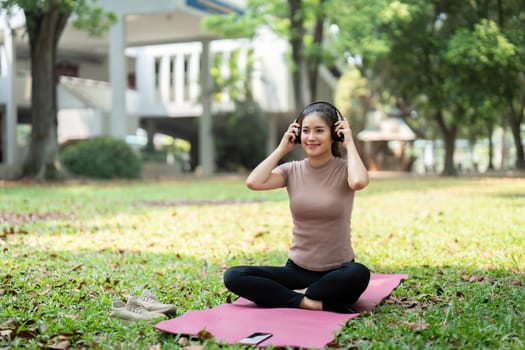 Amidst a lush environment, a woman sits comfortably, enjoying meditation with music, cultivating mindfulness as part of her wellness routine.