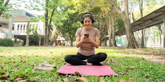 Practicing mindfulness and technology balance, a woman sits cross-legged in a park, integrating digital resources into her wellness routine.