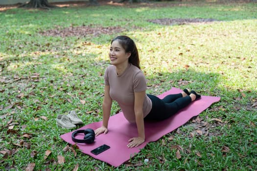 A smiling woman enjoys her yoga practice in an outdoor setting, embodying wellness and routine, reinforcing her physical and mental health.