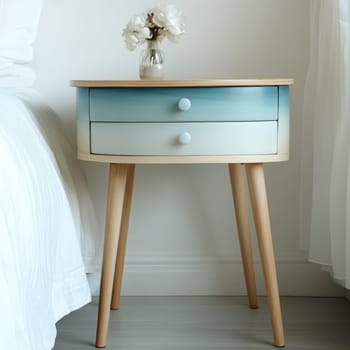 A charming bedside table features a smooth gradient paint design, complemented by a small vase with delicate flowers. The table enhances the bright, airy feel of the room.