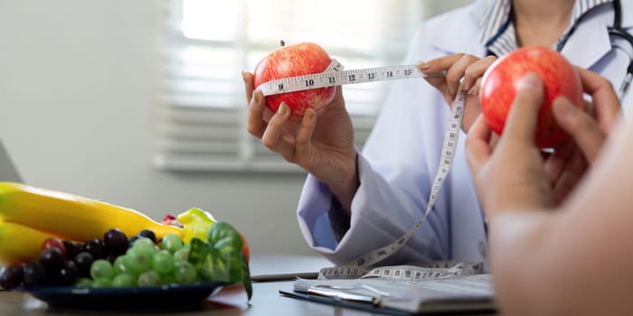 During a consultation, a nutritionist uses a measuring tape around apples to educate her patient on portion size and healthy eating practices.