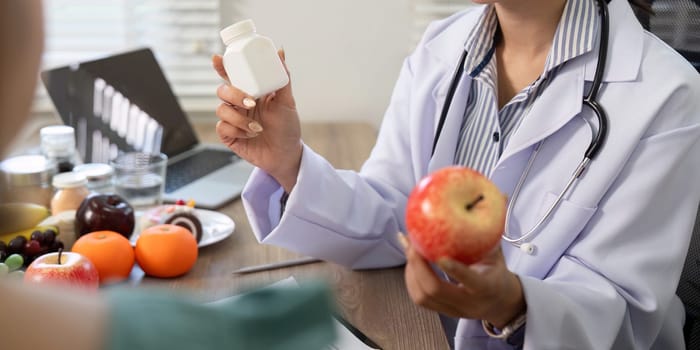 A nutritionist compares a red apple with a supplement bottle, emphasizing the importance of choosing natural foods for health and wellness during a consultation.