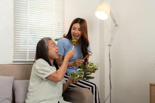 The mother and daughter share laughter while munching on a colorful salad, emphasizing the importance of wellness in their daily life.