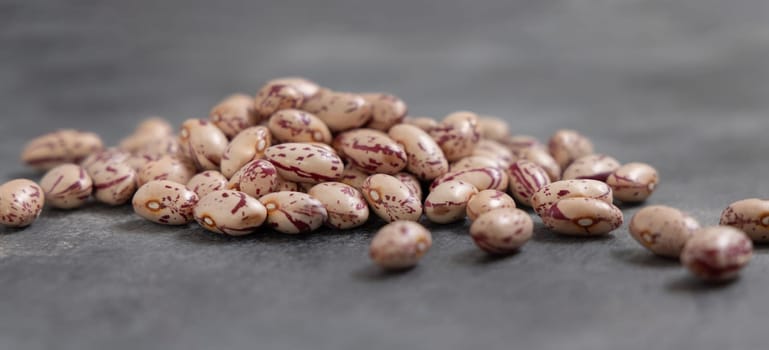 Pile of dried pinto beans on gray table closeup. Healthy vegetarian food, legumes protein source. Traditional Latin American cousin ingredient