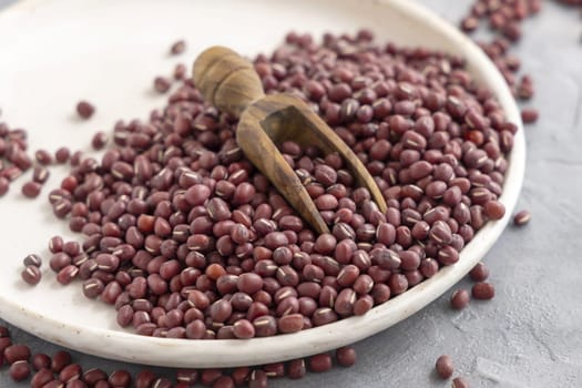 Ceramic plate full of dried red azuki beans with a wooden scoop closeup. Healthy vegetarian food, legumes protein source. Traditional East Asian cousin ingredient